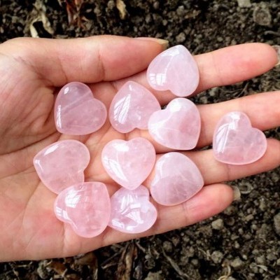 Nove corações de cristal rosa na mão sobre terra escura