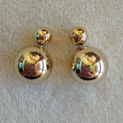 Brincos dourados de esferas lisas com reflexos em fundo branco texturizado