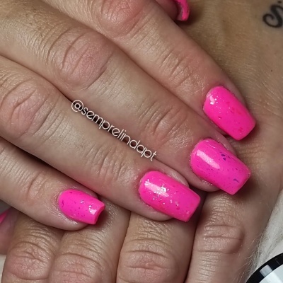 Unhas com verniz rosa fluorescente e partículas brilhantes em mãos com pele clara