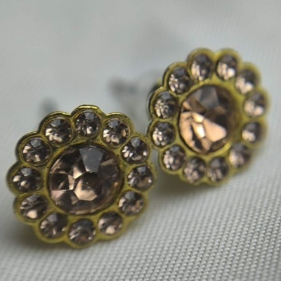 brincos flor dourados com pedras transparentes sobre tecido cinzento