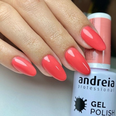 Unhas com verniz gel coral brilhante segurando frasco de verniz andreia professional.