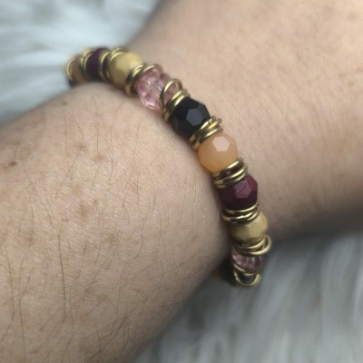 Pulseira com contas facetadas de várias cores e anéis dourados num pulso