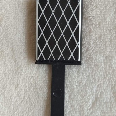 Produto retangular preto com padrão branco em losango, cabo preto, sobre tecido felpudo branco