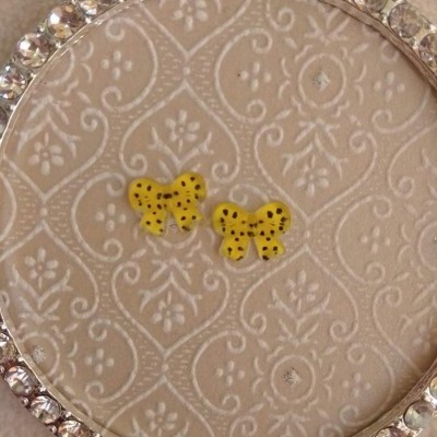 Brincos amarelos em forma de borboleta com pontos pretos num suporte decorativo claro com pedras brilhantes.