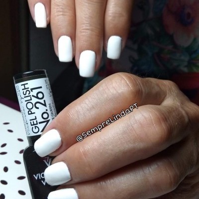 Mãos com unhas brancas pintadas segurando frasco de verniz gel preto