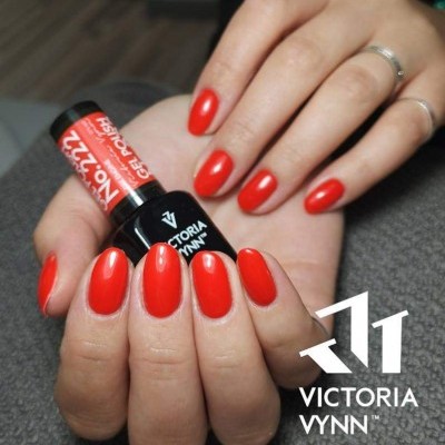 Mãos com unhas vermelhas segurando verniz VICTORIA VYNN em fundo cinzento