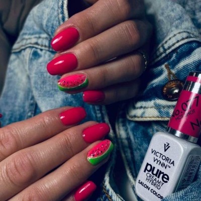 Unhas pintadas de rosa vibrante com decoração de melancia e frasco de verniz em tecido ganga