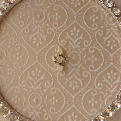 Botão dourado com cristais em tecido beige bordado e aro cravejado de pedras