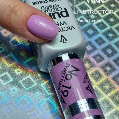 Frasco de verniz gel lilás Victoria Vynn com unha pintada lilás sobre fundo holográfico colorido