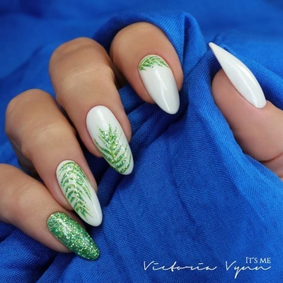 Unhas compridas com decoração verde em fundo branco sobre tecido azul