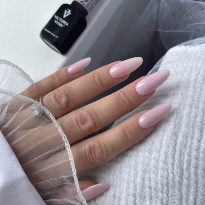 Unhas postiças rosa claro em mão feminina com frascos de verniz gel ao fundo