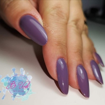 Mão feminina com unhas roxas alongadas de verniz brilhante sobre fundo branco e logotipo B. Unik Nail design.