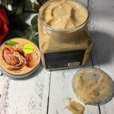 Frasco aberto com creme bege granuloso e tampa com imagem de nozes e etiqueta amarela