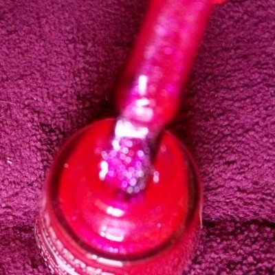 Frasco aberto de verniz de unhas vermelho com pincel embebido em verniz sobre superfície roxa