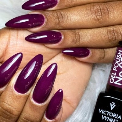 Mãos com unhas roxas brilhantes e frasco de verniz gel Victoria Wynn.