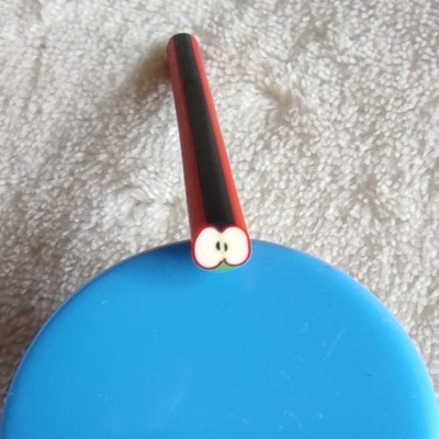 Caneta vermelha e preta com ponta em forma de maçã sobre fundo azul e pano branco.