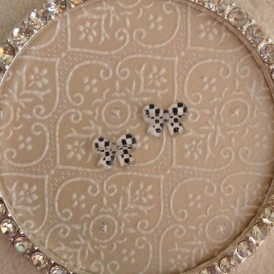 Brincos de laço xadrez preto e branco sobre fundo bege com padrão floral e moldura com pedras brilhantes