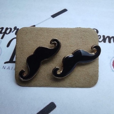 Brincos pequenos em forma de bigode preto com contorno dourado em cartão castanho.