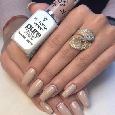 Mãos femininas com unhas esmaltadas em bege claro segurando vernizes Victoria Vynn.