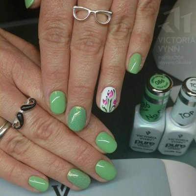 Unhas pintadas de verde com desenho floral, mãos com anéis, frascos de verniz ao fundo