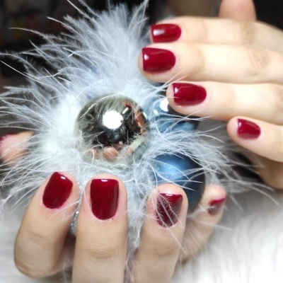 Mãos com unhas vermelhas seguram esfera prateada com penas brancas.