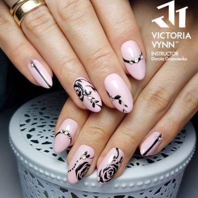 Unhas artísticas rosa claro com desenhos pretos e strass em mãos femininas sobre superfície branca rendada