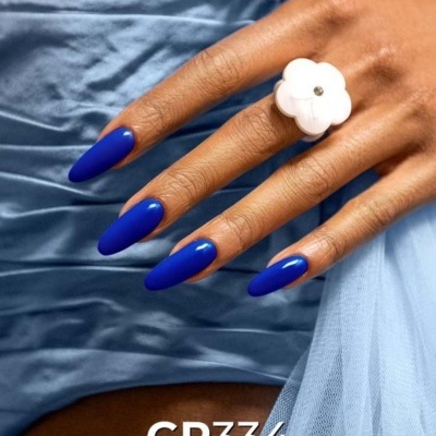 Mão com unhas azuis e anel branco sobre fundo de tecido azul