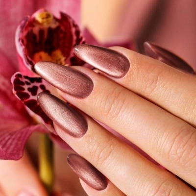 Unhas com verniz metálico bronze segurando orquídea rosa