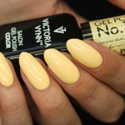 Unhas pintadas com verniz gel amarelo pastel brilhante segurando frasco de verniz