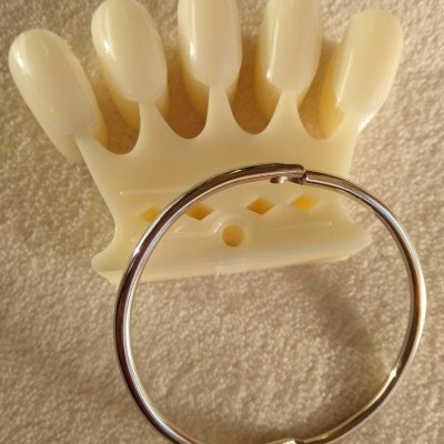 Amostras de unhas em plástico creme e anel metálico prateado sobre tecido branco