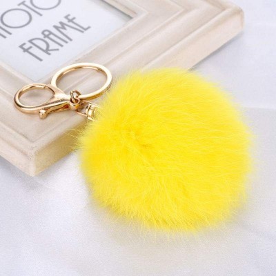 Chaveiro com pompom amarelo felpudo e argola dourada em metal sobre superfície branca