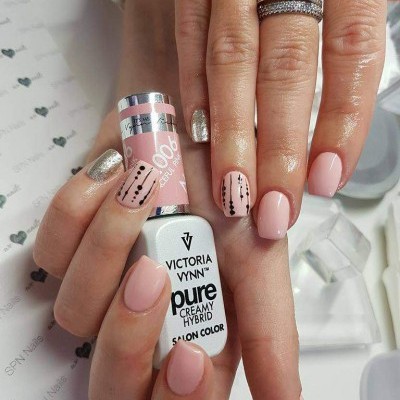 Mãos com unhas decoradas de rosa e dourado segurando frasco de verniz Victoria Vynn