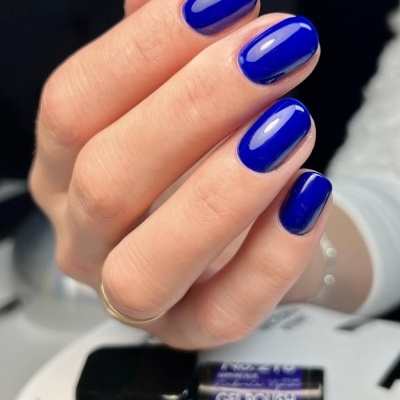 Mão com unhas pintadas de verniz gel azul e frascos de verniz gel no fundo
