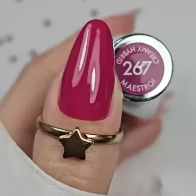 Unha pintada com verniz magenta brilhante e anel dourado com estrela preta a segurar verniz