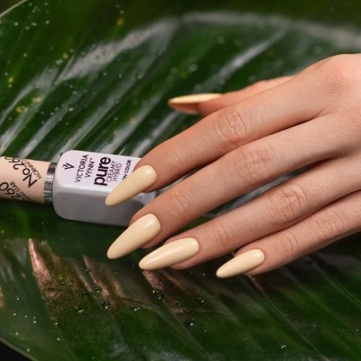 Mão com unhas pintadas de bege claro e frasco de verniz na folha verde