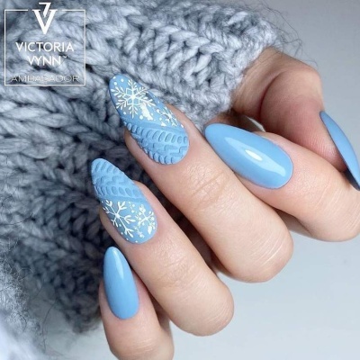 Unhas azuis claras com padrões de camisola de malha e flocos de neve brancos