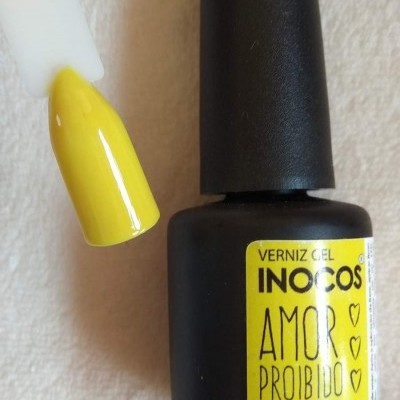 Frasco preto fosco de verniz gel amarelo com amostra de cor numa unha artificial branca
