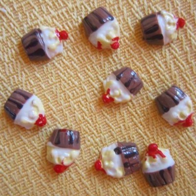 Botões de cupcakes com cobertura branca, base castanha e cereja vermelha sobre tecido amarelo