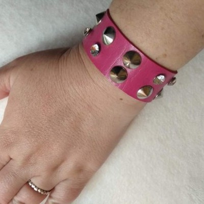 Pulseira de couro rosa com tachas metálicas prateadas no pulso de uma mão