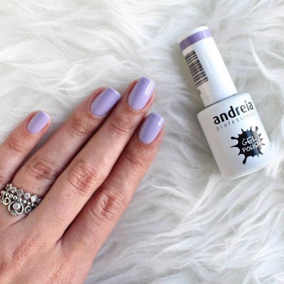 Mão com unhas lilás pintadas e frasco de verniz gel branco e lilás sobre fundo branco felpudo