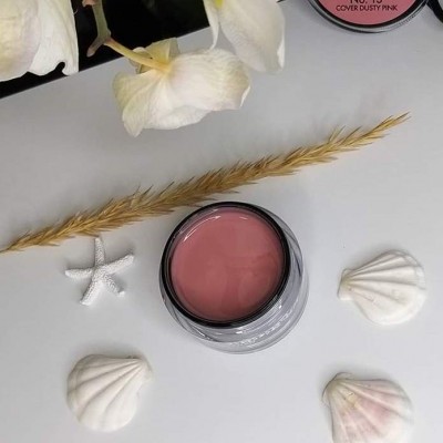 Gel para unhas rosa em pote com tampa preta, flores, espiga seca e conchas sobre superfície branca.