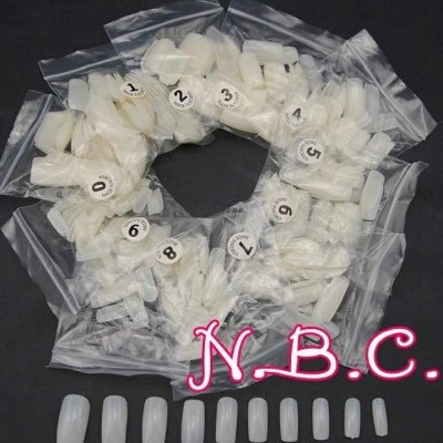 Conjunto de unhas postiças brancas de vários tamanhos em sacos plásticos transparentes, dispostas em círculo com etiqueta N.B.C.