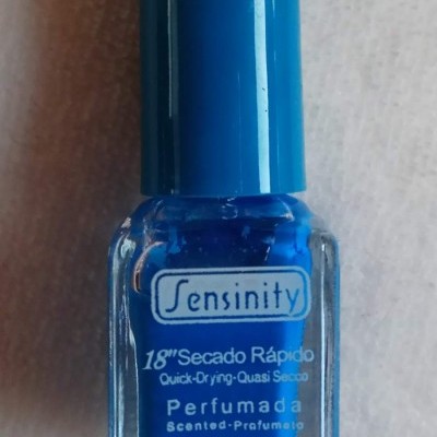 Frasco de verniz de unhas azul com tampa azul e rótulo com texto em várias línguas