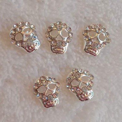 Cinco acessórios prateados em forma de caveira com pedras brilhantes
