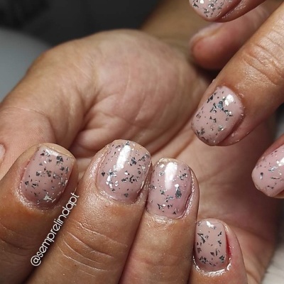 Unhas pintadas com verniz nude e glitter prateado em acabamento brilhante e formato quadrado curto