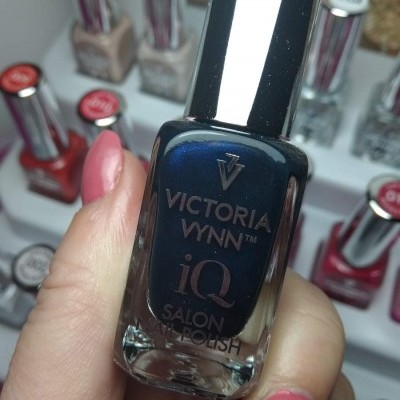 Frasco de verniz de unhas azul escuro da Victoria Vynn iQ Salon Nail Polish segurado por mão com unhas pintadas de rosa