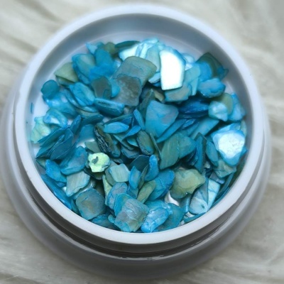 Pedaços pequenos de madrepérola azul e verde em recipiente branco