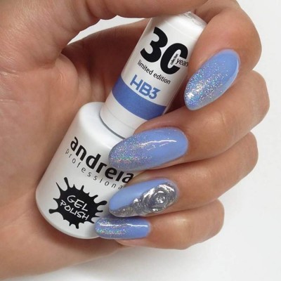 Frasco de verniz gel branco segurado por mão com unhas azuis e glitter, uma unha prateada decorada