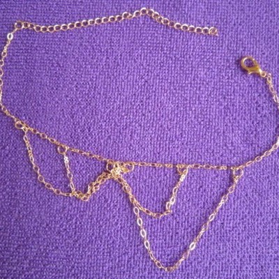 Colar dourado em correntes finas sobre fundo roxo texturizado