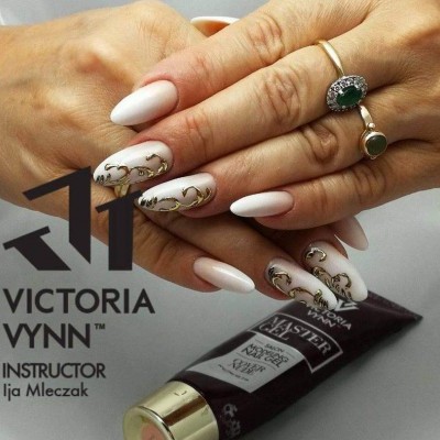 Unhas com verniz branco e detalhes dourados sobre tubo de cosmético roxo